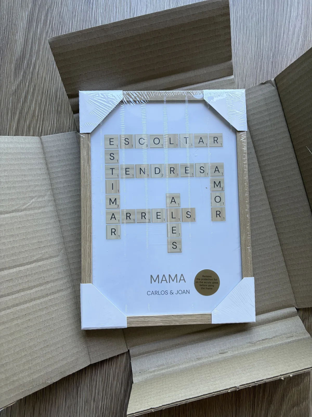 Cuadro personalizado con nombres estilo Scrabble en marco negro, colgado en dormitorio — regalo de boda